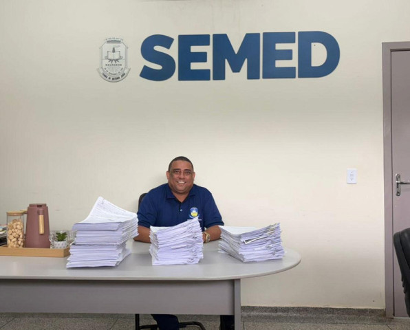 Secretário municipal de Educação, Nilson Francisco da Silva, ao lado de pilhas de contratos que com a digitalização serão coisas do passado. Foto: Divulgação/Assecom